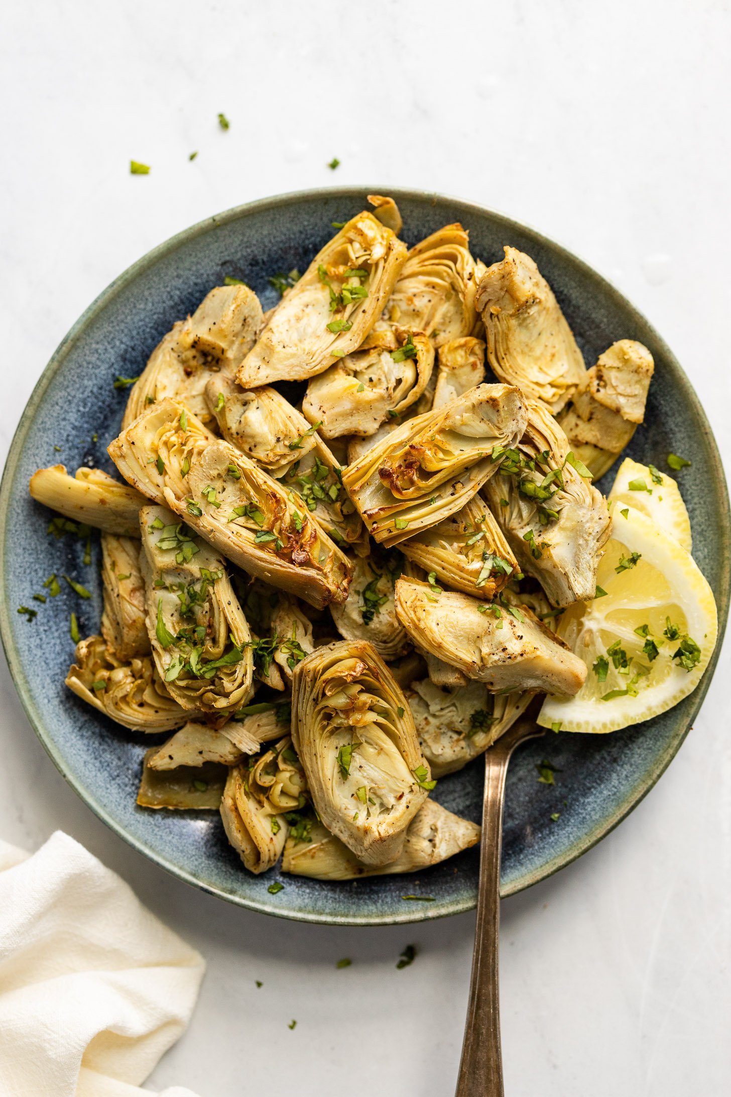 Plate of air fryer frozen artichoke hearts with parsley and lemon.
