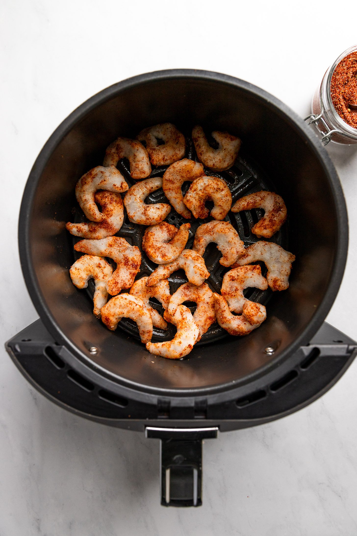 Shrimp in air fryer basket before cooking tossed with cajun spice.