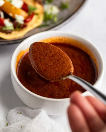 Spoon scooping fajita sauce next to plate of fajitas.