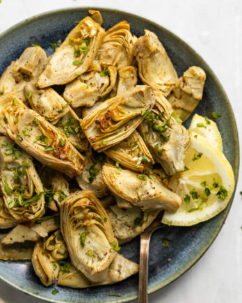 Plate of air fried artichoke hearts with serving fork and lemons.