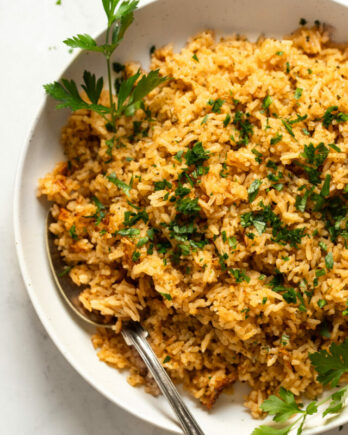Bowl of seasoned rice with parsley and serving spoon.