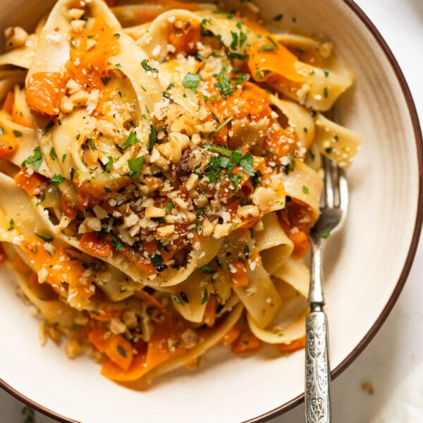 Up close bowl of carrot pasta with carrot ribbons topped with walnuts and parsley.