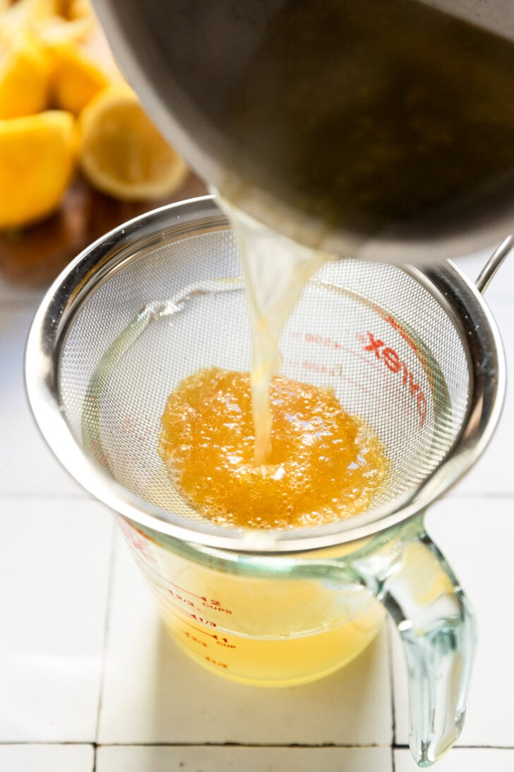 Lemon syrup pouring into fine mesh sieve separating out the lemon zest.