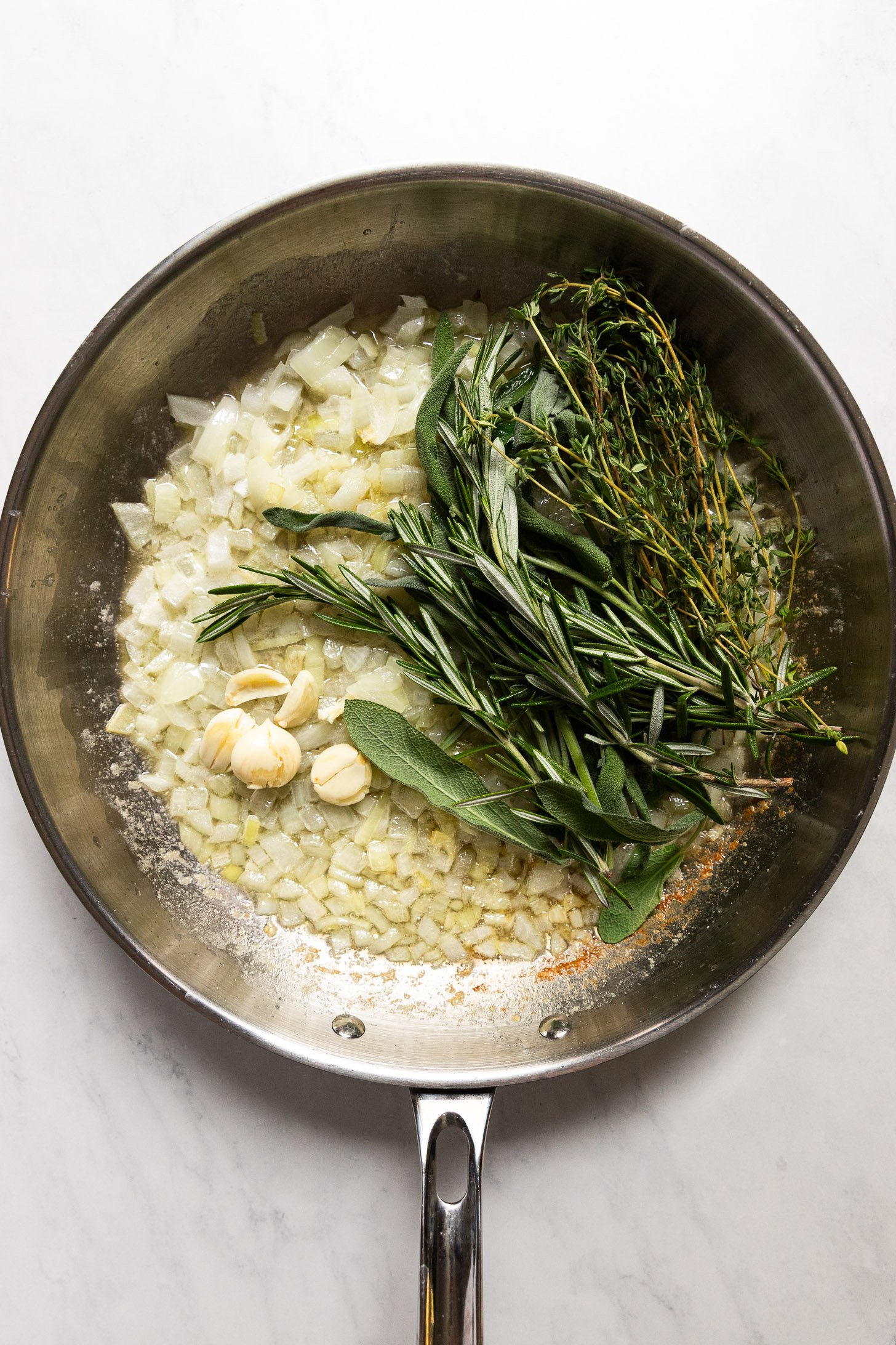 Sprigs of herbs and smashed garlic added to skillet.