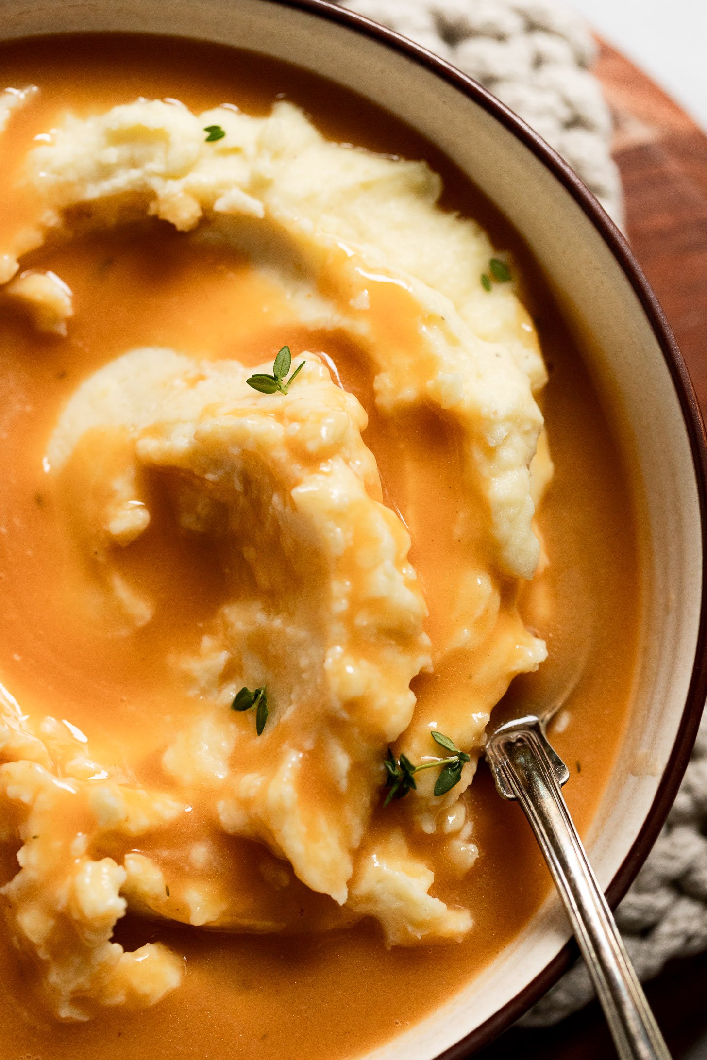 Bowl of mashed potatoes with vegetarian gravy and fresh thyme.
