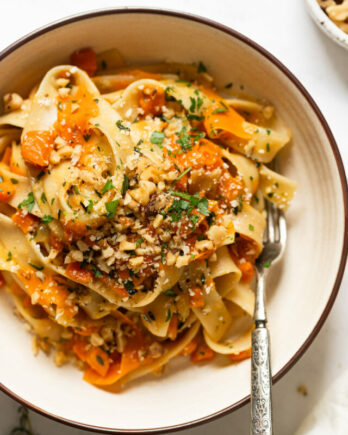 Up close bowl of carrot pasta with carrot ribbons topped with walnuts and parsley.