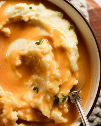 Bowl of mashed potatoes with vegetarian gravy and fresh thyme.