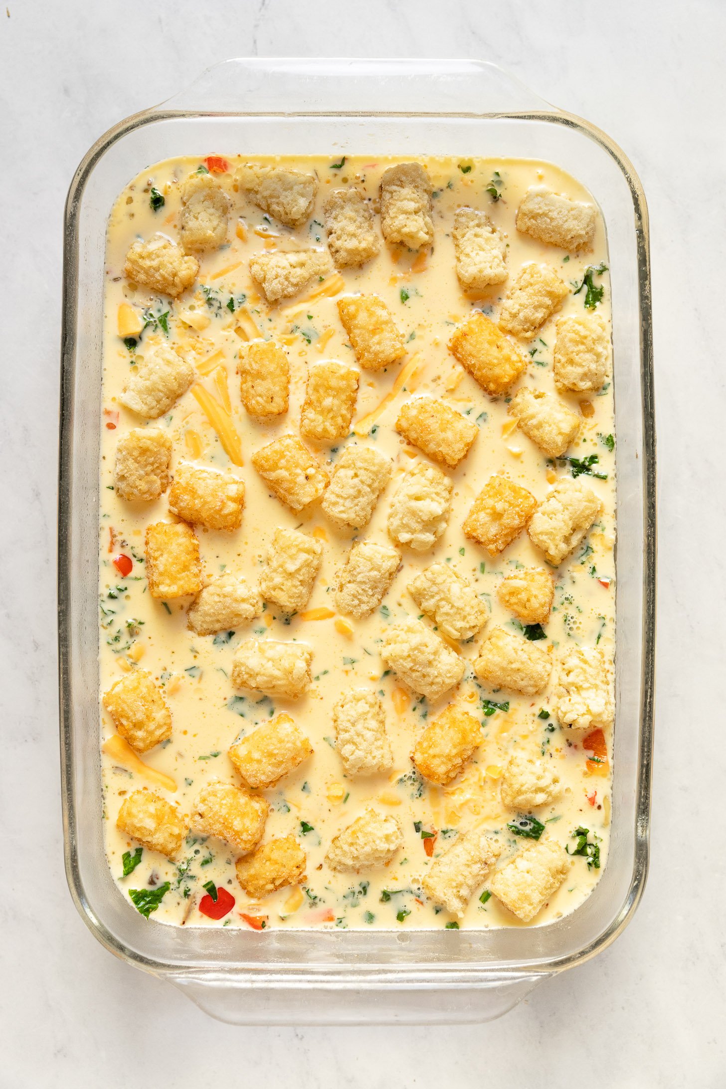 Breakfast casserole with tater tots on top before baking.