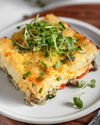Square of breakfast casserole on plate topped with microgreens.