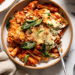 Bowl of baked ziti with basil leaves.
