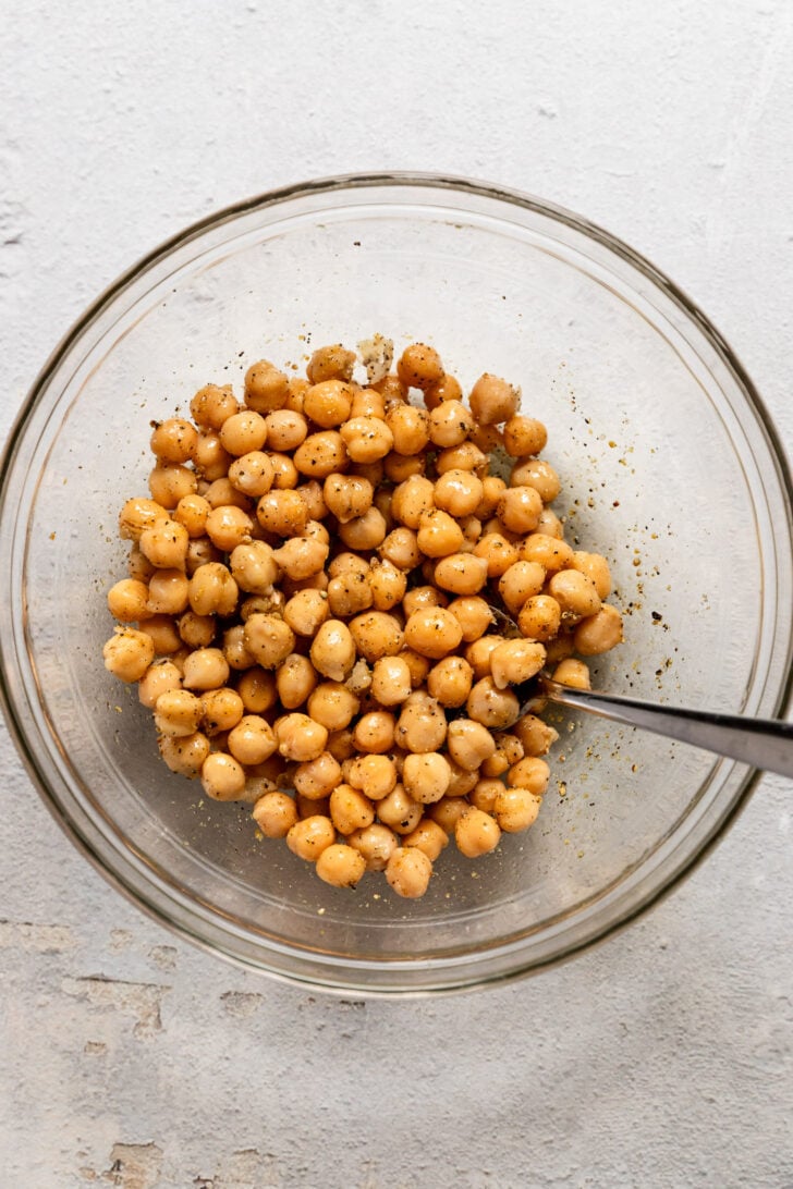 Chickpeas stirred with seasoning in bowl with spoon.