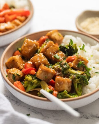 Side view of bowl of tofu stir fry with fork and rice.
