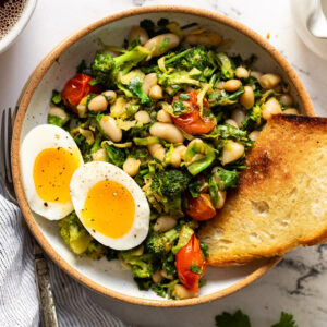 Bowl of broccoli, kale, white beans with soft boiled egg halves and toast.