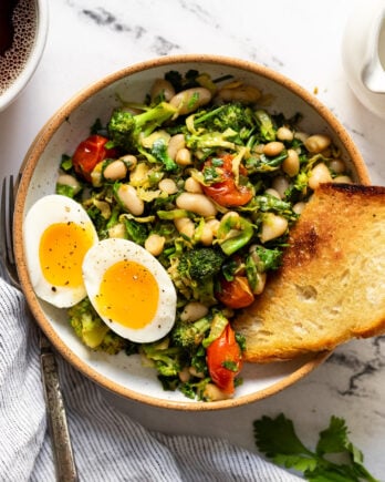 Bowl of broccoli, kale, white beans with soft boiled egg halves and toast.