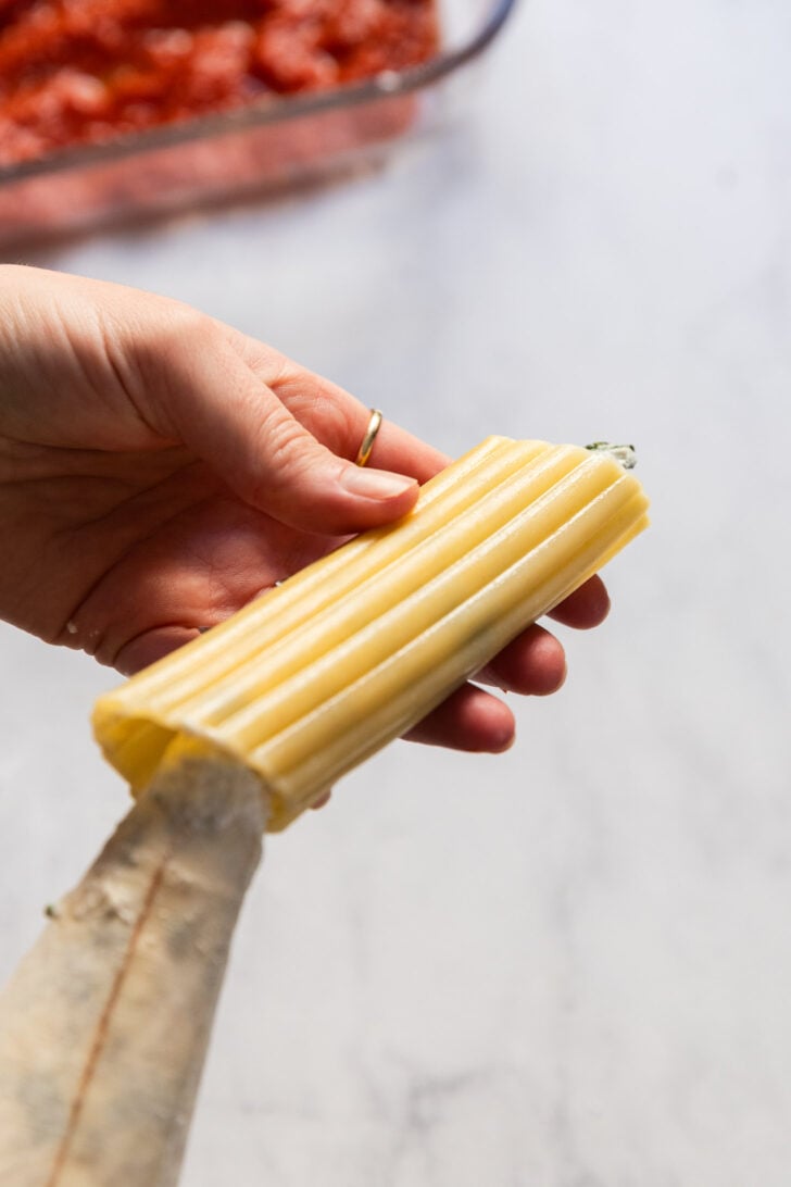 Hand holding noodle and filling it using a pastry bag.