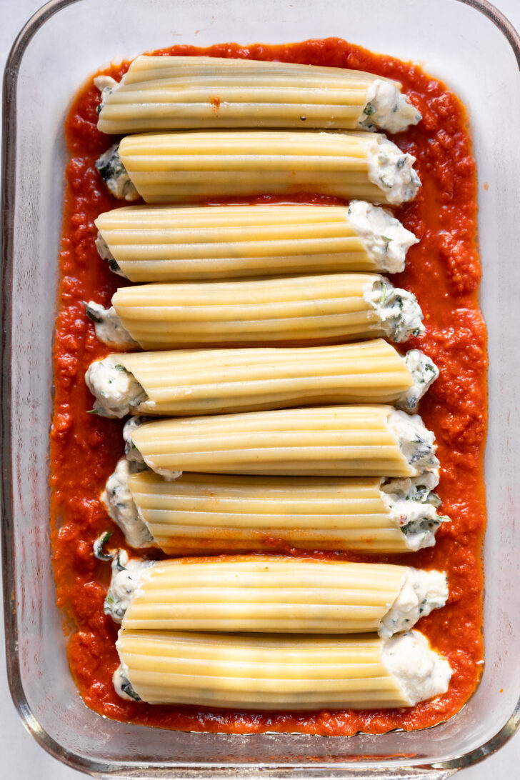 Filled manicotti in dish on top of pasta sauce.