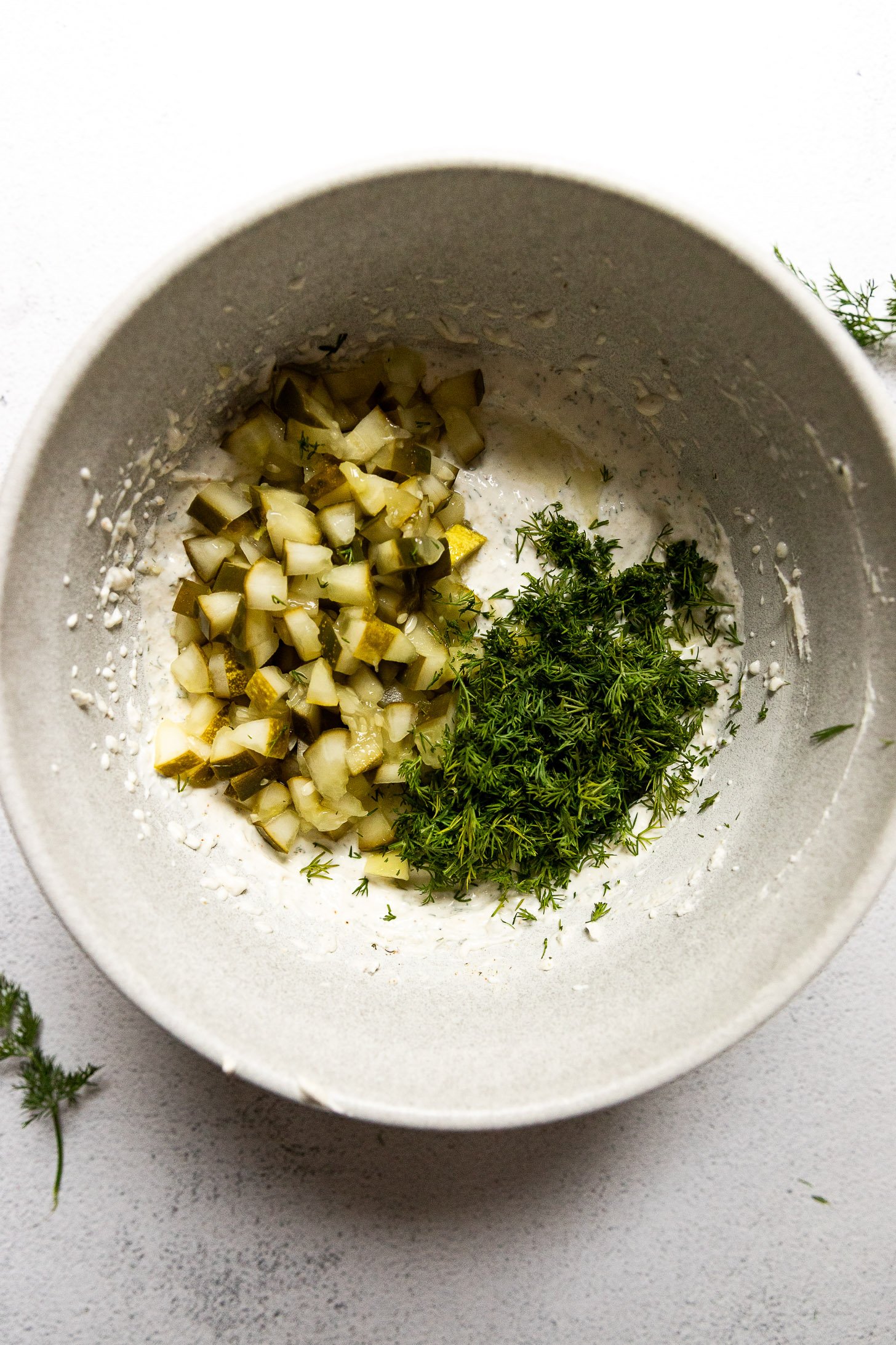 Mixing bowl of dip with chopped pickles and dill on top