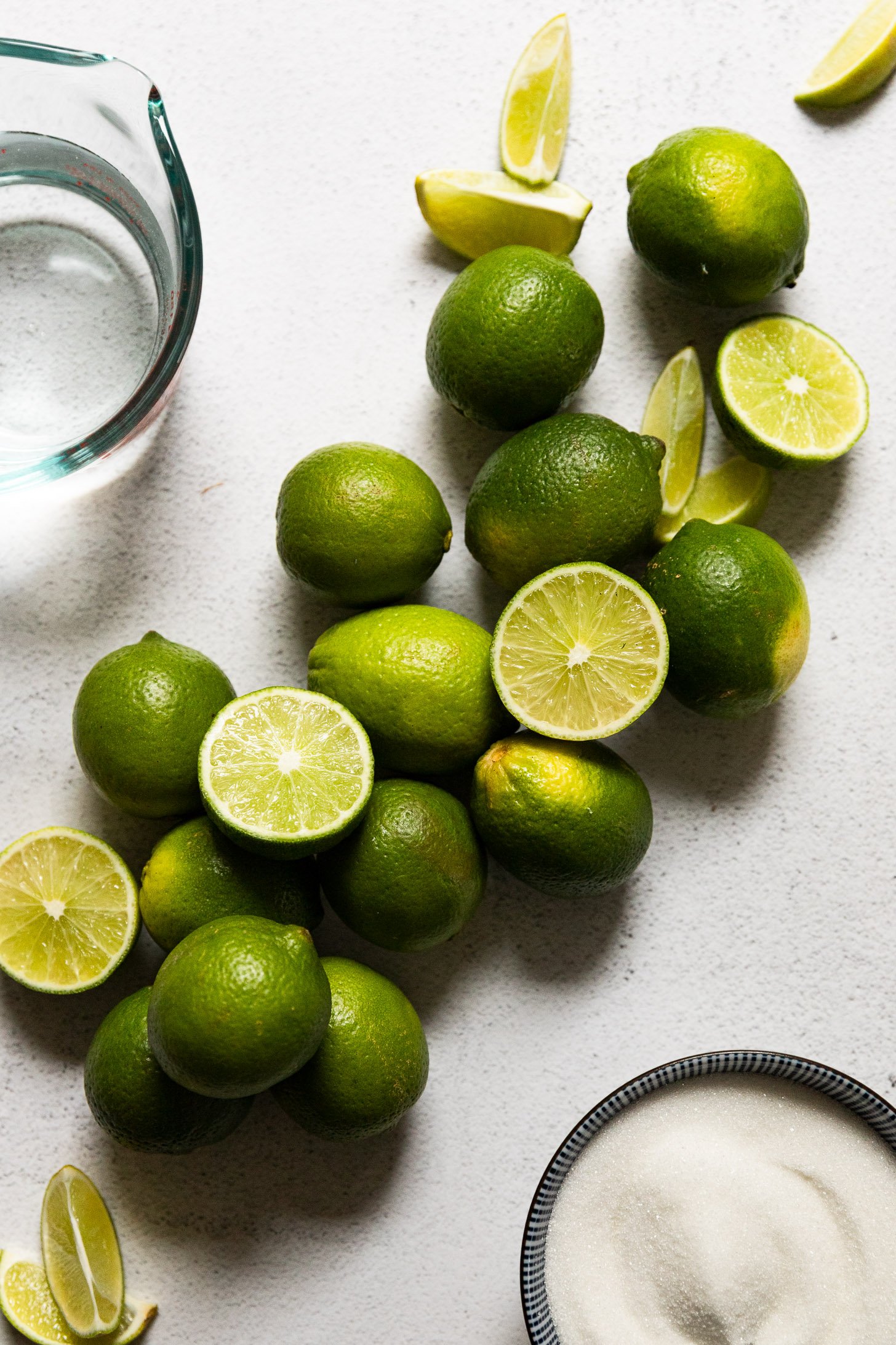 Whole and cut limes next to lime juice and sugar.