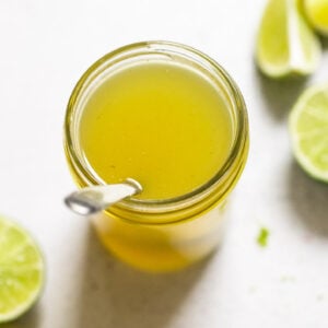 Jar of lime syrup with spoon next to lime wedges.