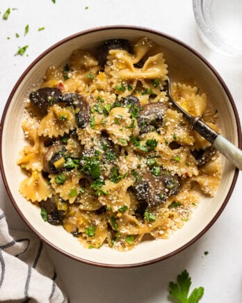 Bowl of bowtie pasta with mushrooms leeks and parsley garnish.