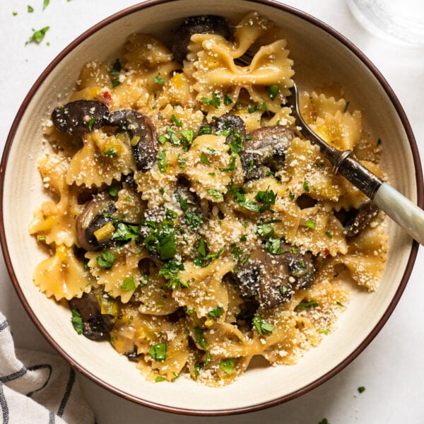 Bowl of bowtie pasta with mushrooms leeks and parsley garnish.