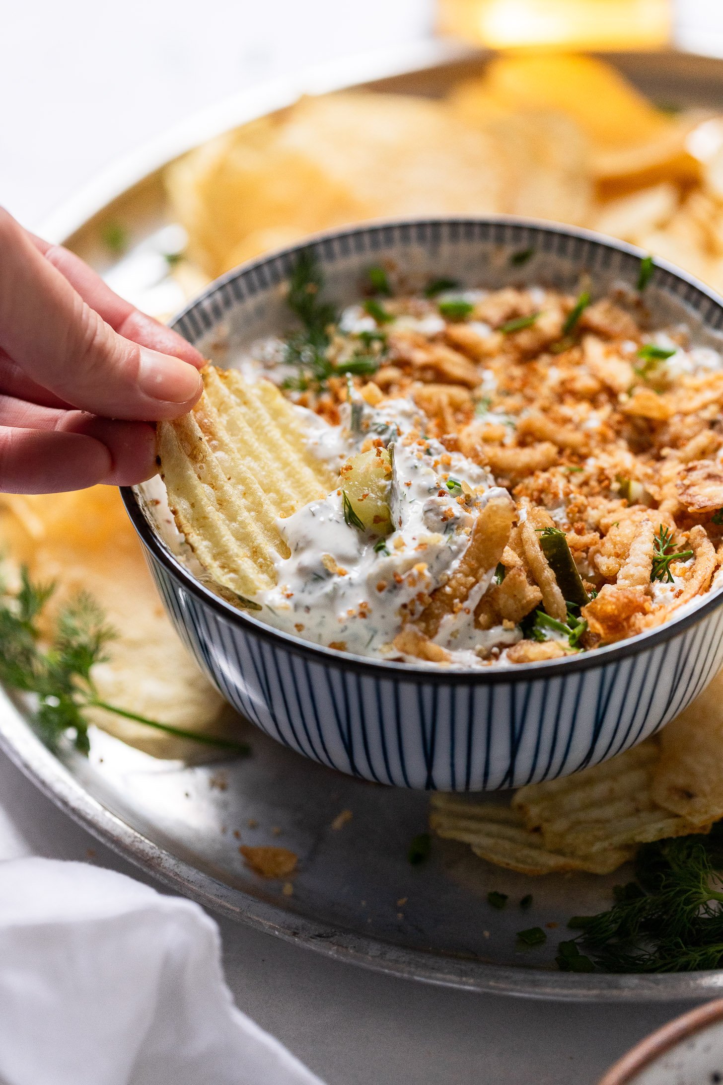 Chip dipping into pickle ranch dip with crispy onions.