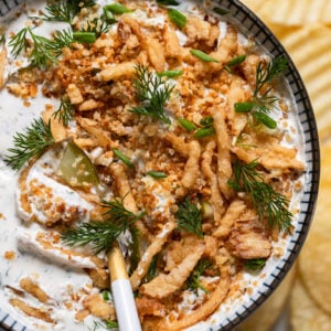Bowl of pickle ranch dip with spoon and fried onions on top.