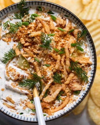 Bowl of pickle ranch dip with spoon and fried onions on top.