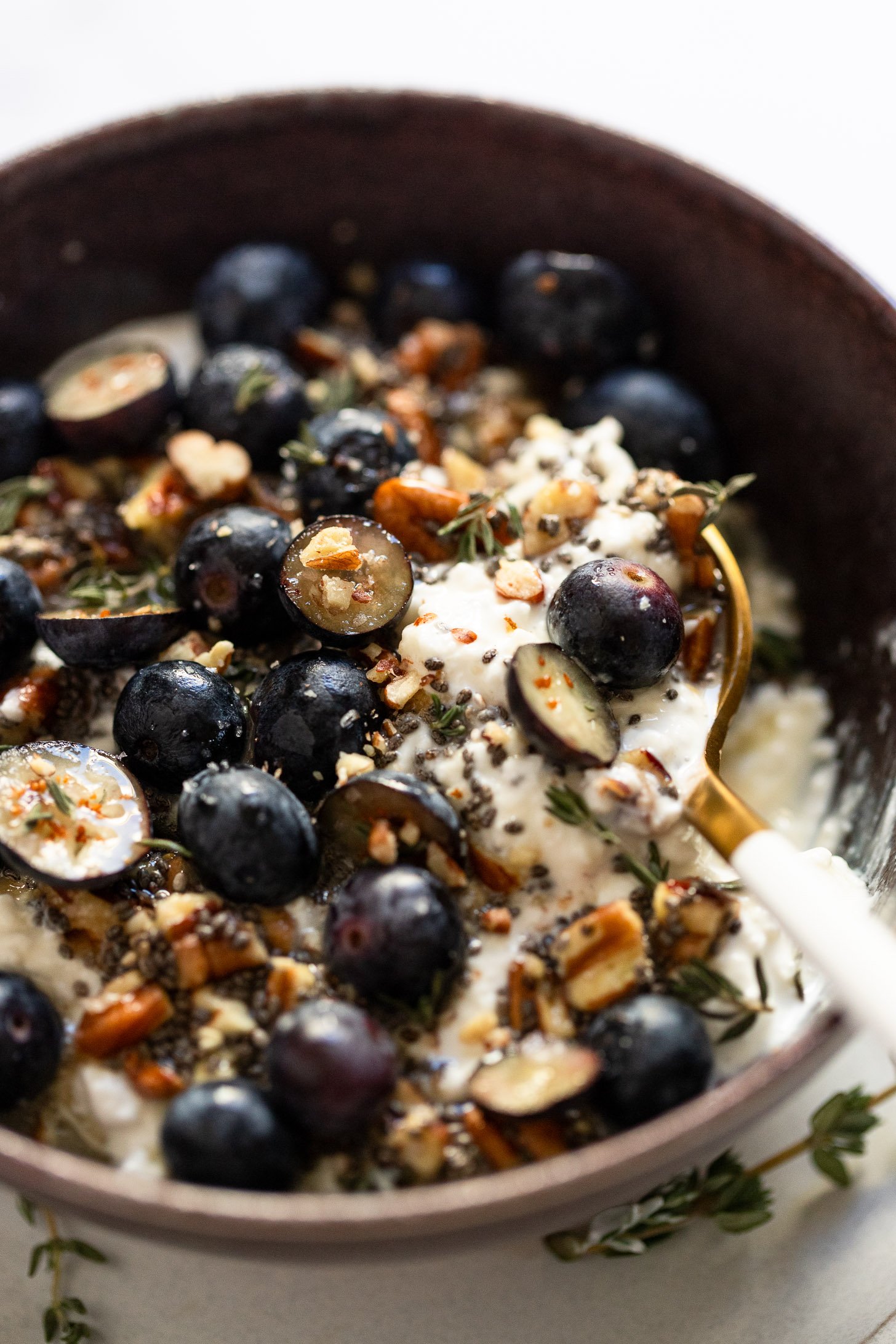 Side view of purple bowl with blueberries and pecans on top of cottage cheese in spoon.