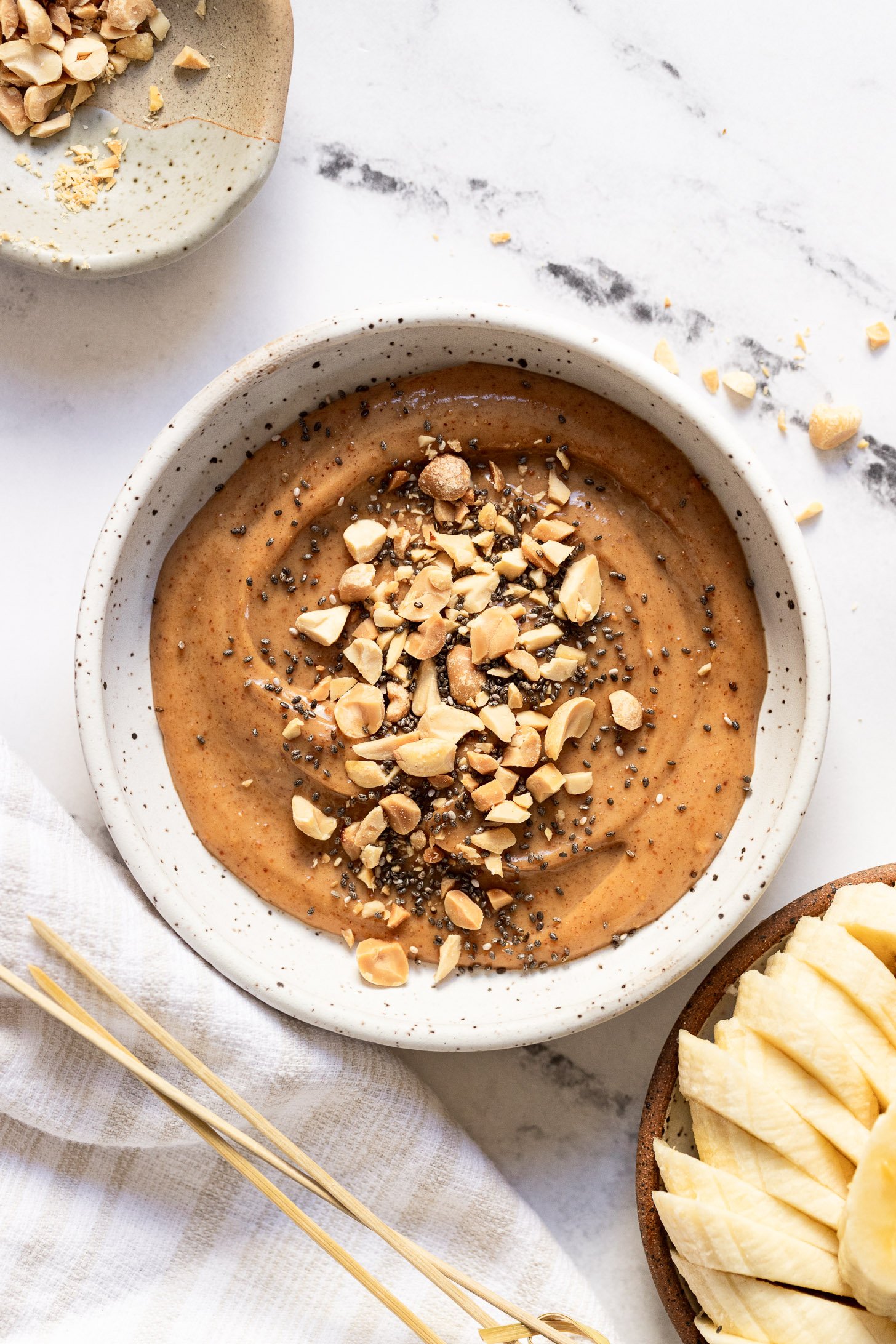 Bowl of peanut butter dip with chopped peanuts and chia seeds.
