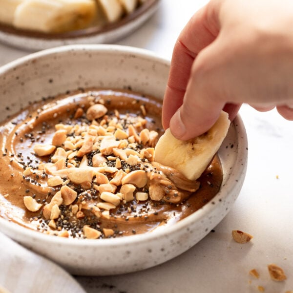 Banana slice dipping into peanut butter dip.