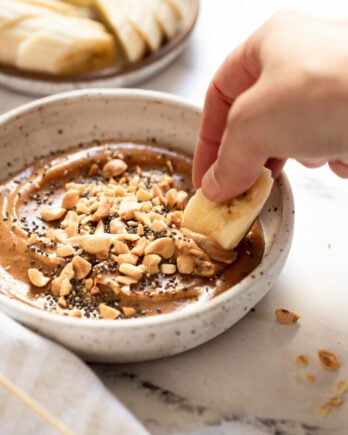 Banana slice dipping into peanut butter dip.